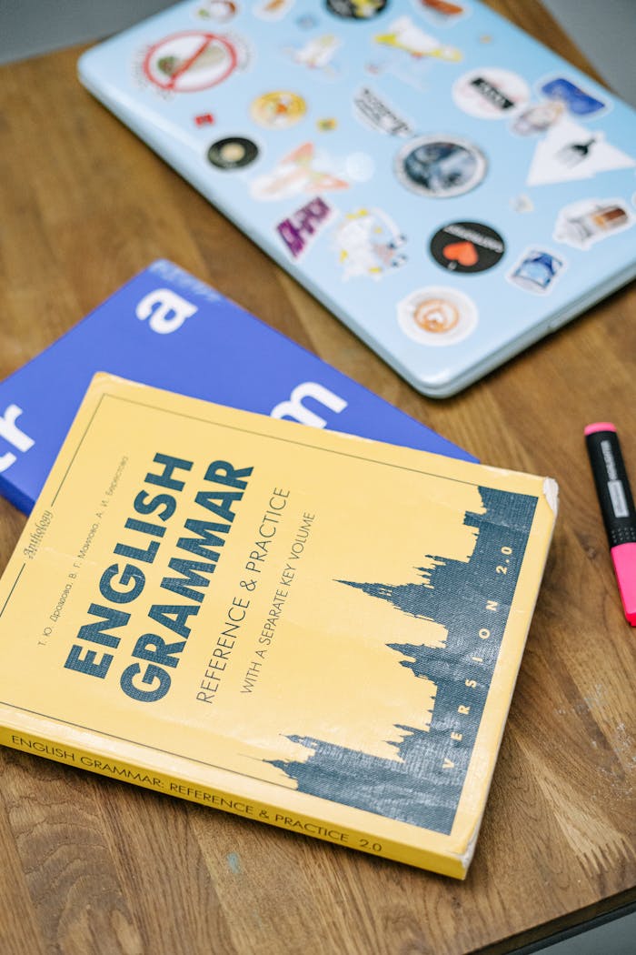 Crafting Captivating Headlines: Your awesome post title goes here High-angle view of an English grammar book and a laptop with stickers on a wooden desk.